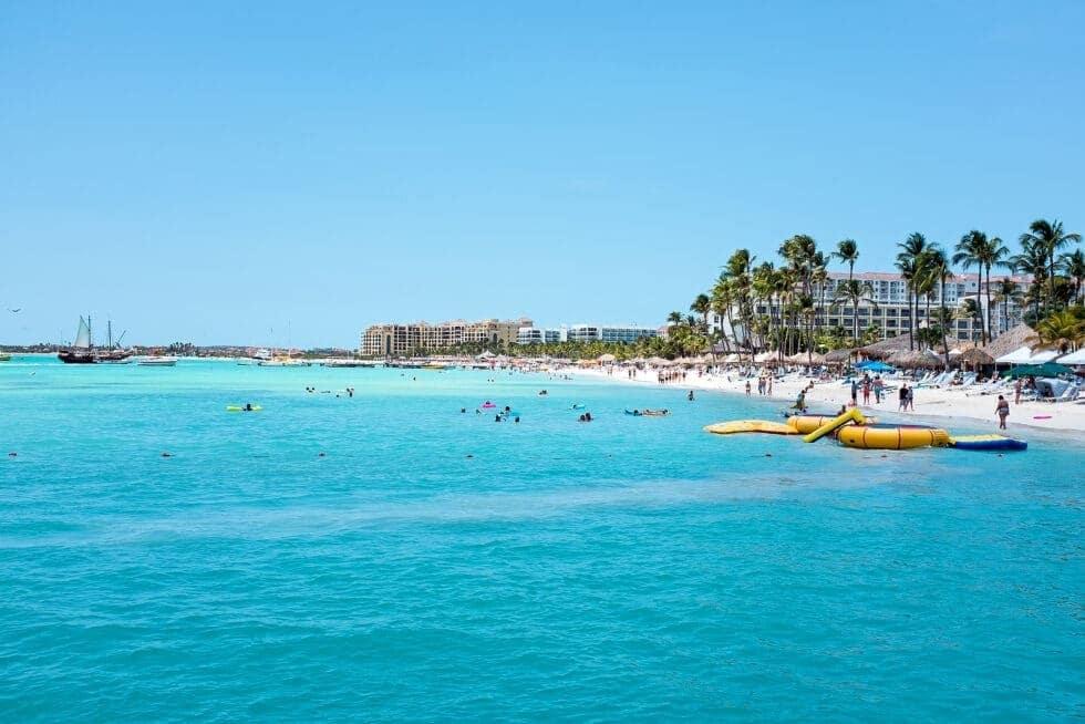 A calm turquoise shoreline in the Bahamas with beachgoers and resort views for Boardwalk Resort Vacations Caribbean destinations.