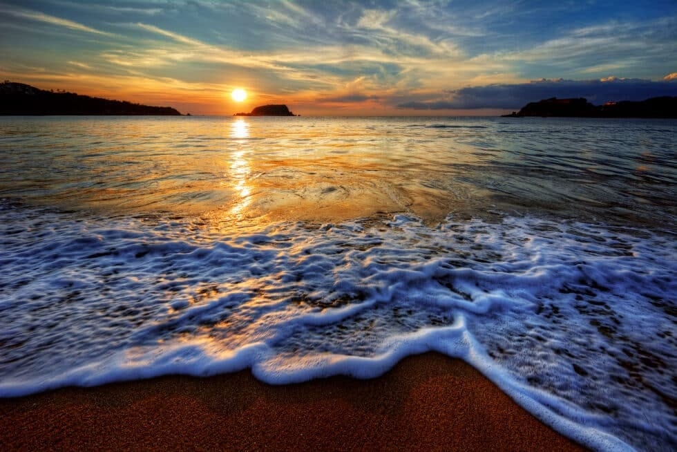 Sunset light washing over a quiet Caribbean shoreline with waves moving across the sand for Boardwalk Resort Vacations Caribbean destinations.